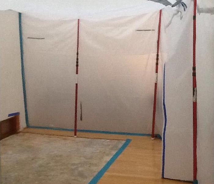 Room with wood floors and plastic sheeting hung with blue and red tape